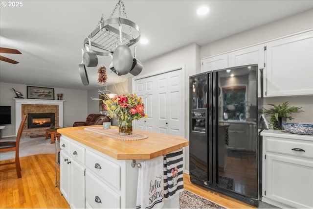 kitchen featuring wooden counters, light wood-style floors, white cabinets, a lit fireplace, and black fridge