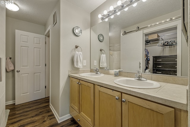 bathroom with double vanity, a textured ceiling, a sink, and wood finished floors