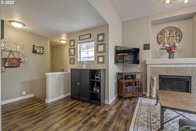 living room with baseboards, a tiled fireplace, and dark wood-type flooring