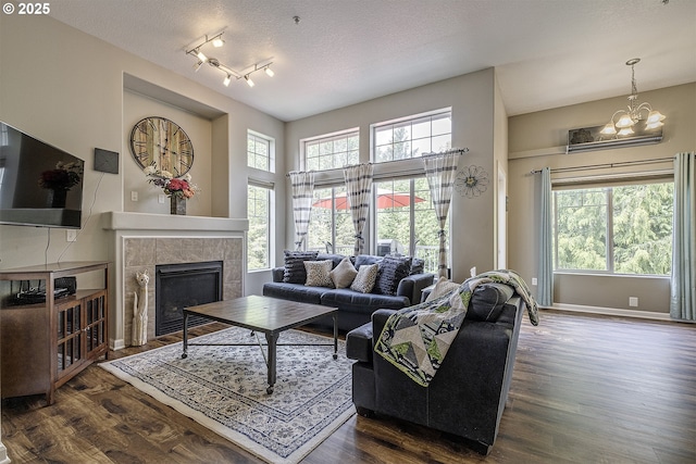 living room with plenty of natural light, dark wood-type flooring, a tile fireplace, and a chandelier