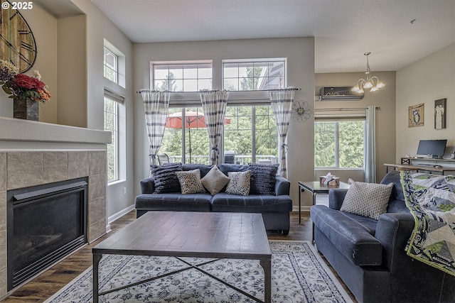 living area featuring a tiled fireplace, baseboards, wood finished floors, and a notable chandelier