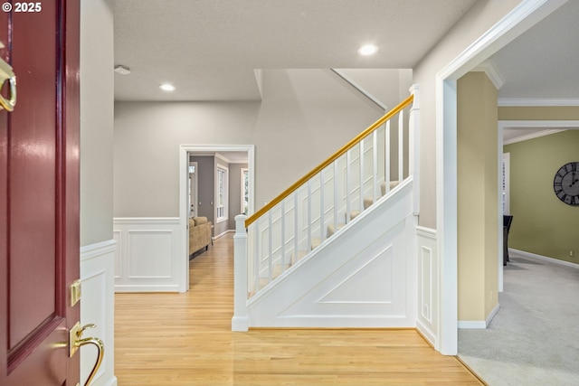 foyer featuring crown molding, wood finished floors, a decorative wall, and stairs