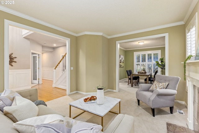 living area featuring light carpet, wainscoting, stairway, crown molding, and a decorative wall