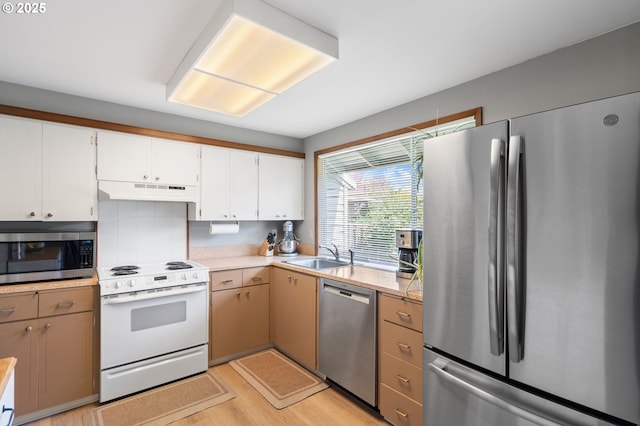 kitchen featuring a sink, light wood finished floors, light countertops, stainless steel appliances, and under cabinet range hood