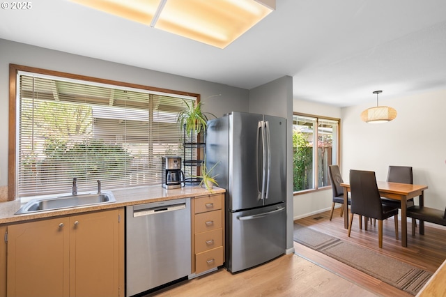 kitchen with decorative light fixtures, a sink, light countertops, light wood finished floors, and stainless steel appliances