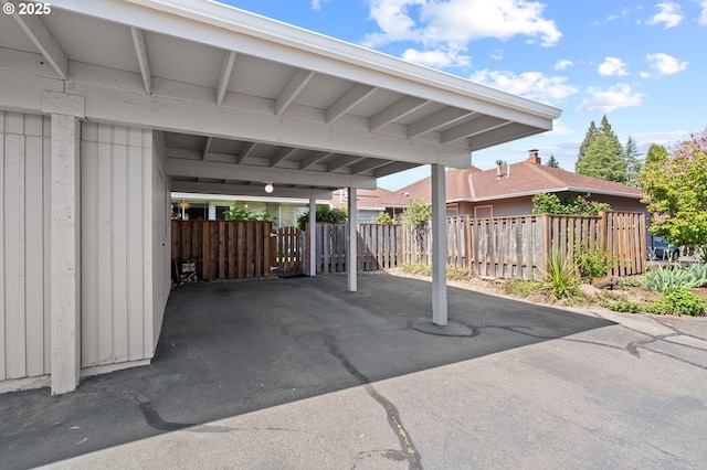 view of vehicle parking featuring aphalt driveway, fence, and a carport
