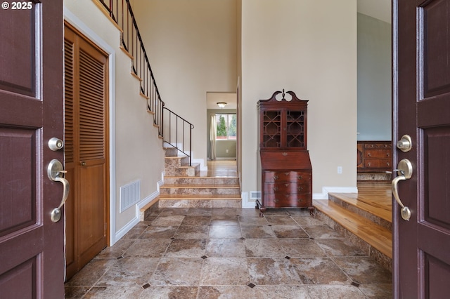 foyer featuring baseboards, visible vents, a high ceiling, and stairs