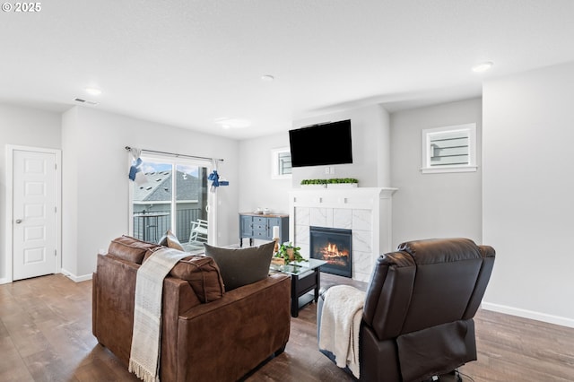 living room featuring wood finished floors, a tile fireplace, visible vents, and baseboards