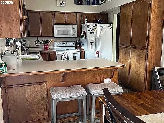 kitchen with white appliances, kitchen peninsula, a breakfast bar, and sink