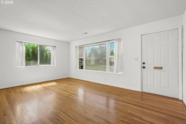 unfurnished living room with hardwood / wood-style flooring, a textured ceiling, and baseboards