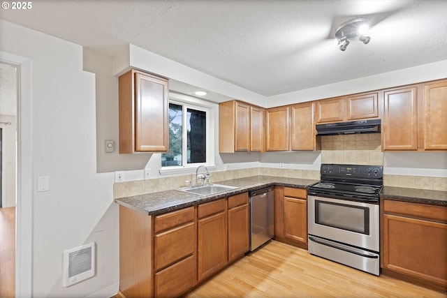 kitchen with light wood-style flooring, a sink, under cabinet range hood, appliances with stainless steel finishes, and dark countertops