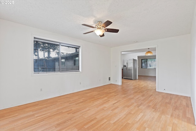 spare room featuring light wood finished floors, baseboards, a textured ceiling, and ceiling fan