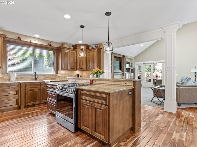 kitchen with decorative columns, stainless steel gas stove, a center island, light stone countertops, and light hardwood / wood-style floors