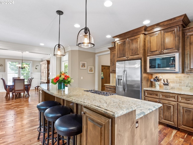 kitchen featuring hardwood / wood-style flooring, appliances with stainless steel finishes, decorative light fixtures, and a kitchen island