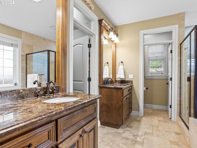 full bathroom with baseboards, two vanities, a sink, a shower stall, and stone finish floor