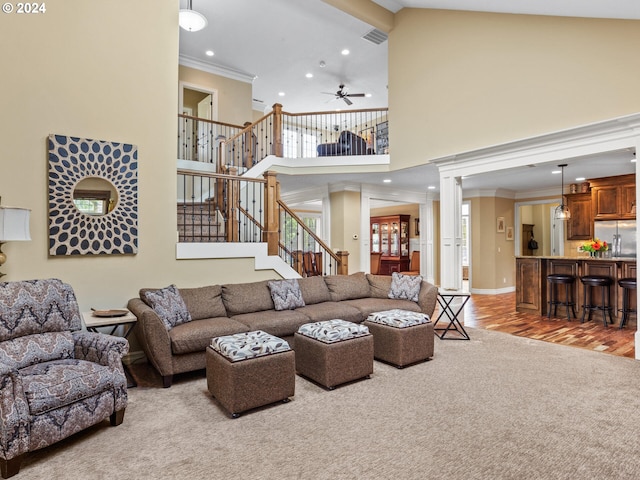 carpeted living area with visible vents, stairway, crown molding, a towering ceiling, and ornate columns