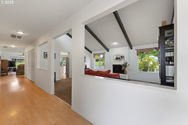 living area featuring visible vents, a large fireplace, wood finished floors, baseboards, and lofted ceiling with beams