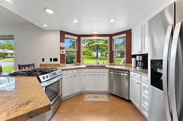 kitchen featuring appliances with stainless steel finishes, white cabinetry, a sink, light countertops, and light wood-style flooring