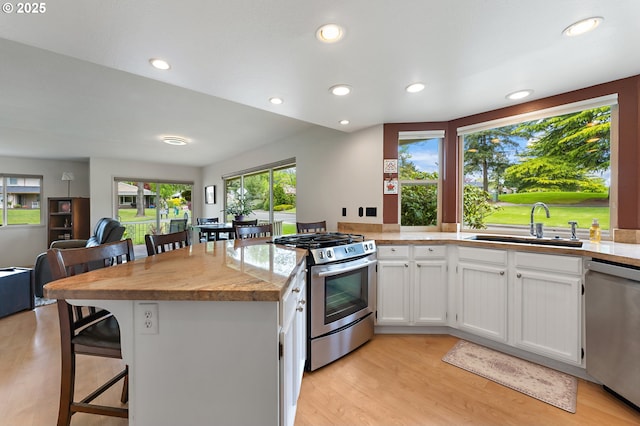 kitchen with a peninsula, a kitchen breakfast bar, white cabinets, a sink, and stainless steel appliances