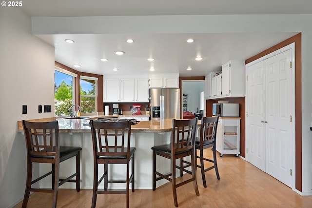 kitchen with appliances with stainless steel finishes, a sink, light wood finished floors, a peninsula, and white cabinetry