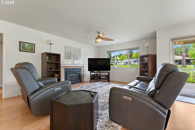 living area with a ceiling fan, a glass covered fireplace, a wealth of natural light, and light wood finished floors
