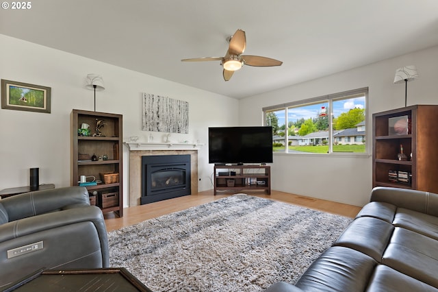 living area with a glass covered fireplace, wood finished floors, and ceiling fan