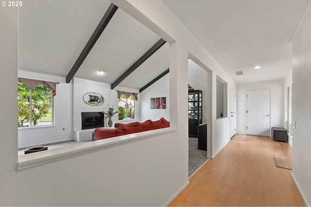 hallway with visible vents, light wood-style floors, plenty of natural light, and vaulted ceiling with beams