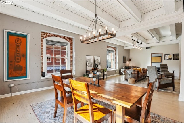 dining area featuring arched walkways, a chandelier, wood finished floors, baseboards, and beam ceiling