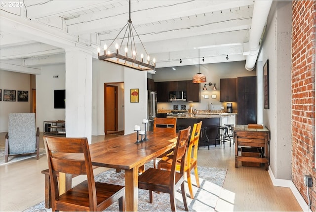 dining room with brick wall, rail lighting, a high ceiling, light wood-style floors, and a chandelier