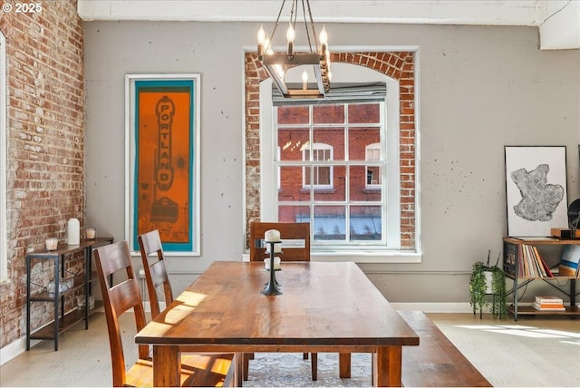 dining area featuring a chandelier, baseboards, brick wall, and wood finished floors