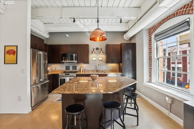 kitchen with a sink, stainless steel appliances, light wood-style floors, a kitchen bar, and beam ceiling