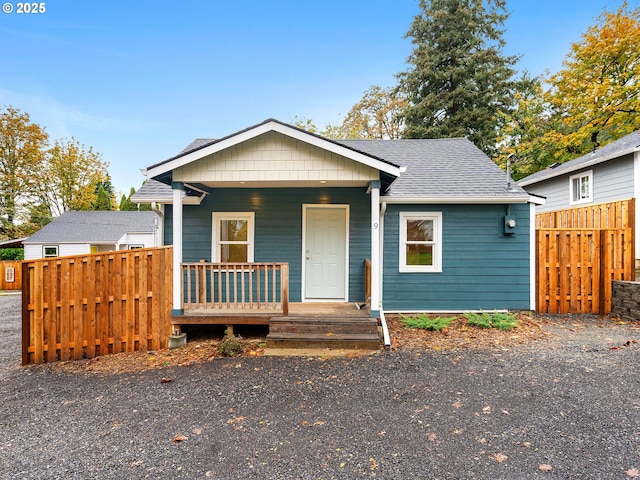 bungalow-style house featuring a porch, a shingled roof, and fence