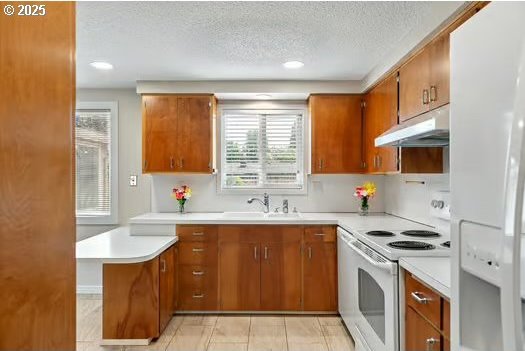 2065 Providence St, Eugene, OR 97401 - kitchen with white appliances, under cabinet range hood, brown cabinets, a textured ceiling, and light countertops
