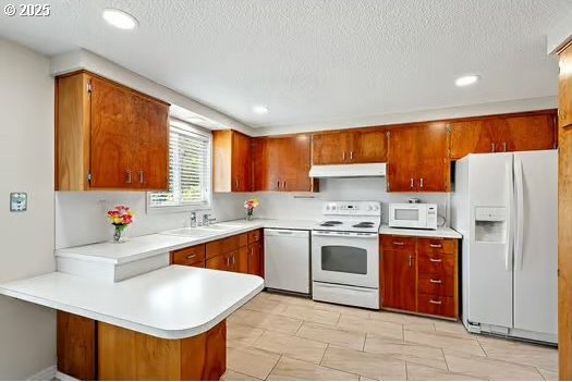 2065 Providence St, Eugene, OR 97401 - kitchen featuring white appliances, under cabinet range hood, a peninsula, light countertops, and brown cabinets