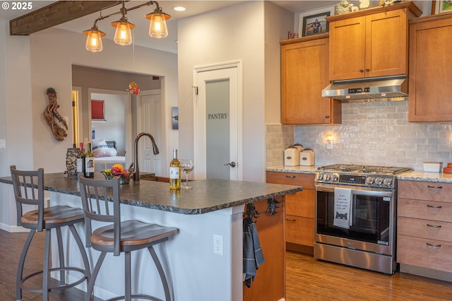 kitchen with dark wood finished floors, tasteful backsplash, under cabinet range hood, brown cabinets, and gas stove