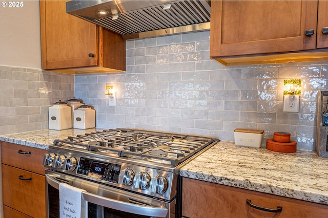 kitchen featuring stainless steel range with gas cooktop, brown cabinets, decorative backsplash, and premium range hood