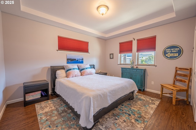 bedroom featuring dark wood finished floors, baseboards, and a tray ceiling