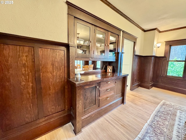 bar area with light wood finished floors, wainscoting, ornamental molding, and a decorative wall