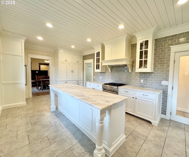 kitchen with crown molding, high end stainless steel range, custom range hood, white cabinets, and a kitchen island