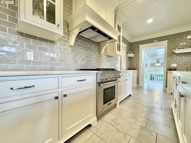 kitchen with high end stainless steel range, custom exhaust hood, light countertops, white cabinetry, and glass insert cabinets