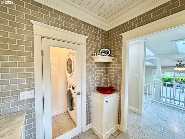 laundry room featuring stacked washing machine and dryer, crown molding, a skylight, baseboards, and a ceiling fan
