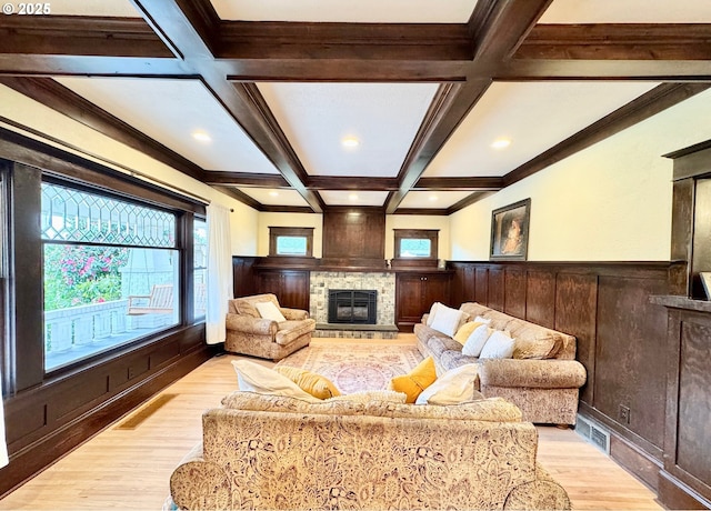 living room featuring light wood-style floors, coffered ceiling, beamed ceiling, plenty of natural light, and wainscoting