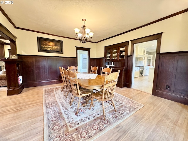 dining room featuring a chandelier, light wood-type flooring, a wainscoted wall, and ornamental molding