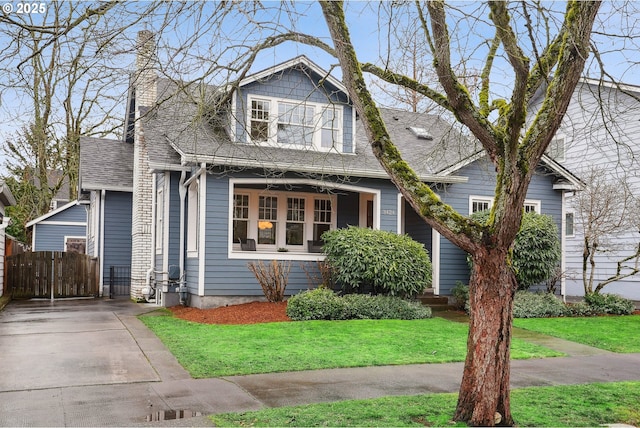 view of front of property with a front lawn, roof with shingles, a chimney, and fence