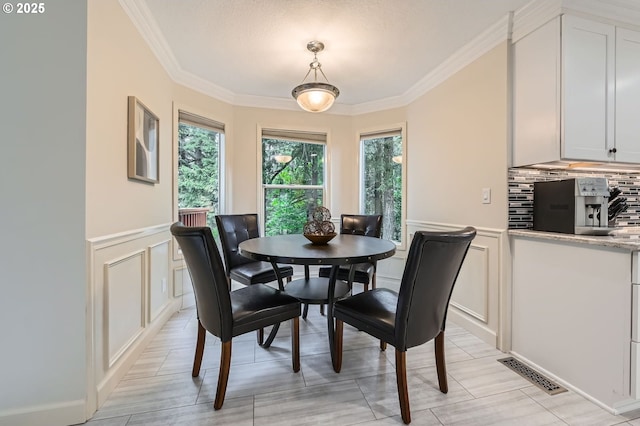 dining area featuring a decorative wall, crown molding, and wainscoting