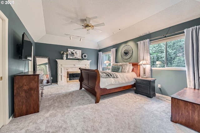 carpeted bedroom with vaulted ceiling, rail lighting, baseboards, a premium fireplace, and a textured ceiling