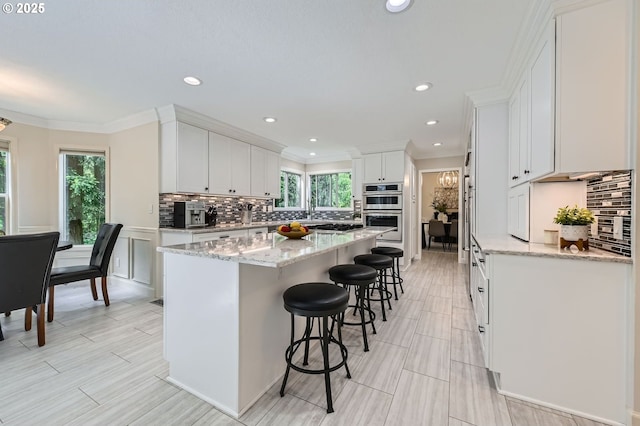 kitchen with appliances with stainless steel finishes, a breakfast bar, white cabinets, a kitchen island, and tasteful backsplash