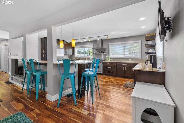703 NW 94th St, Vancouver, WA 98665 - kitchen with open shelves, wall chimney range hood, dark brown cabinetry, a kitchen breakfast bar, and wood finished floors