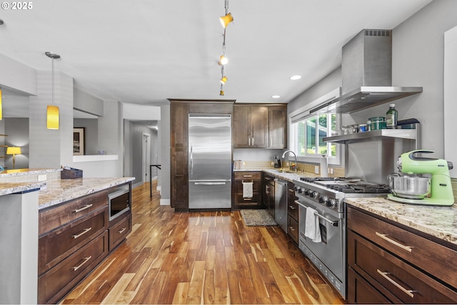 703 NW 94th St, Vancouver, WA 98665 - kitchen with built in appliances, wall chimney exhaust hood, wood-type flooring, decorative light fixtures, and dark brown cabinets