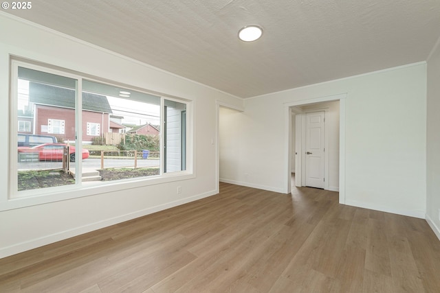 spare room featuring crown molding, a textured ceiling, and light wood-type flooring